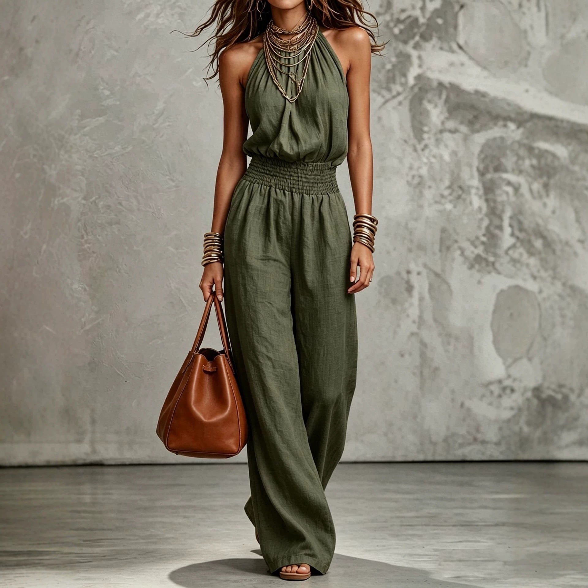 Woman wearing a green jumpsuit holding a brown leather bag against a textured wall.